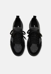 Černé a šedé sportovní boty s texturovanou tkaninou a tkaničkami, s logem na vnitřní straně podešve, zobrazené z nadhlavního pohledu.