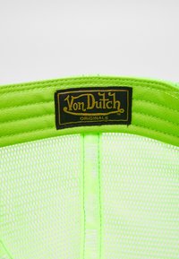Neon zaļš tīkla cepure ar melnu un zelta Von Dutch logo. Sānā ir viegli zaļa teksts "HIGH ON LIFE". Strukturēts dizains.