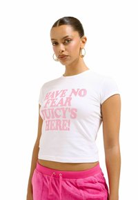 T-shirt court blanc avec un texte en paillettes roses audacieux qui dit "N'AYEZ PAS PEUR JUICY EST LÀ !", avec des manches courtes et une coupe ajustée.