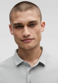 Grijze polo met korte mouwen en een kraag, voorzien van een gladde textuur, twee knopen en een getailleerde pasvorm. Eenvoudig ontwerp zonder patronen.