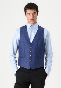 Colete azul texturizado com cinco botões, duas bolsos frontais, usado sobre uma camisa azul clara. Ajuste slim e design ajustado.