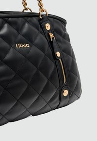 Zwarte, gewatteerde lederen handtas met goudkleurige hardware, voorzien van een ritsvak en het merkembleem. De kettinghengsels zorgen voor een gedetailleerde accent.