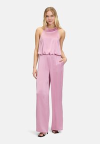 Roze jumpsuit met een halternek, zachte drapering bij de taille en een wijde pijpdesign. Beschikt over twee zijzakken en een gladde textuur.