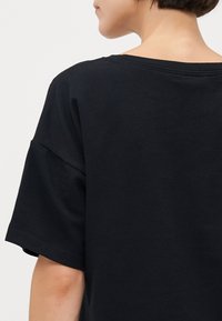 Svart bomull t-skjorte med avslappet passform, drop shoulder-design og vid halslinning. Jevn tekstur og enkel stikking rundt halsen.