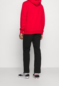 Sudadera roja, pantalones negros y zapatillas de cuadros. La sudadera tiene un bolsillo tipo canguro, corte relajado y puños acanalados.