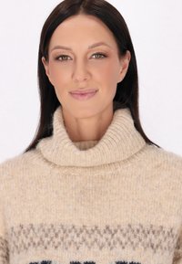 Pulover tricotat bej cu un guler înalt, cu tivuri, și detalii cu model în culori maro închis și albastru pe piept. Textură moale, croială lejeră.