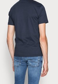 T-shirt corto color blu navy scuro con collo a giro, realizzato in morbido cotone. Indossato con jeans in denim azzurro chiaro, dotati di tasche posteriori e dettagli di cuciture.