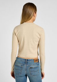 Beige ribbet langtærmet top med rund hals, parret med lyseblå denimjeans med en mærket læderlap på taljen.