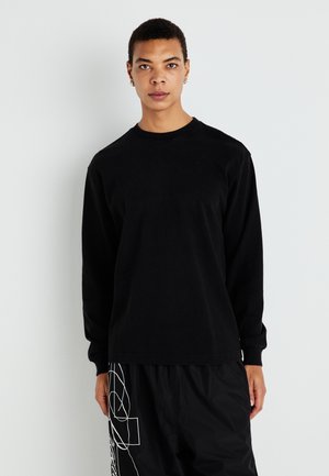Black long-sleeve t-shirt in cotton with a crew neckline. Slim fit with stitched hems. The model wears loose black pants with white lines.