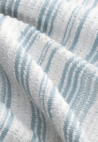Tissu rayé en blanc et bleu clair, présentant un motif de tricot texturé avec des points variables et une apparence douce et aérienne.