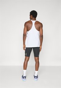 Athletic outfit featuring a white sleeveless tank top and black fitted shorts, with contrasting accents and blue athletic shoes.