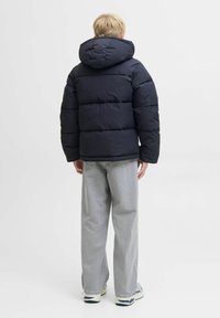 Marineblå pufferjakke med hætte, der har en quiltet design, tyk polstring og elastiske manchetter, parret med lysegrå vide jeans og sneakers.
