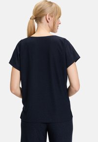 Marineblaue Kurzarmbluse mit rundem Ausschnitt und lockerer Passform. Der Stoff hat einen subtilen Schimmer. Die Rückansicht zeigt eine glatte Textur und den Saum.