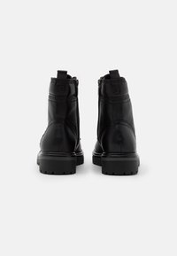 Botas de tobillo de cuero negro con un acabado suave, cierre de cremallera y tacones texturizados. Presentan acentos de costura y una suela de goma resistente.