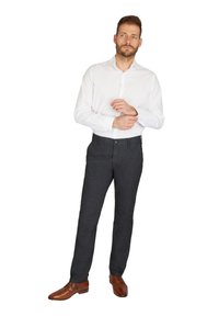 Weißes Langarmhemd, dunkle strukturierten Hose und braune Lederschuhe. Das Outfit sitzt gut und hat einen Knopfdetails an der Hose.