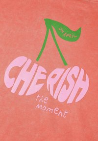 Koraal stof heeft een grafisch ontwerp met twee roze kersen en groene stelen. De tekst luidt "KOESTER het moment" in dikke letters.
