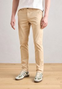Beige chinos med smal passform, med flat front og sidelommer. Kombinert med flerfargede joggesko med grønne, grå og hvite detaljer.