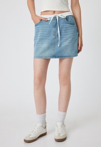 Falda de mezclilla en azul claro con cintura elástica y cordón blanco. Cuenta con dos bolsillos frontales y un corte recto. Estilo casual.