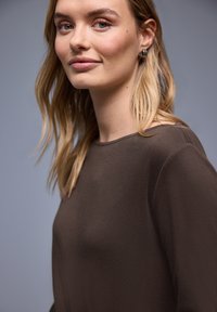 Bruine top met hoge hals, gemaakt van zacht materiaal met een gladde textuur, met een losse pasvorm en minimale stikdetails.