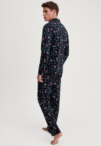 Langärmeliges Pyjama-Set aus schwarzem Stoff mit einem bunten, festlichen Muster von Nussknackern, Schneeflocken und Bändern. Legere Passform, weicher Stoff.