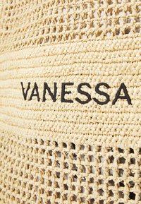 Gewoven stro materiaal in een natuurlijke beige kleur, voorzien van een zwart geborduurd "VANESSA" logo en een bet tekstuur open geweven patroon.