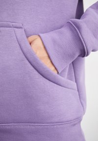 Lila sweatshirt med känguruficka och ribbade ärmar, tillverkad av mjukt tyg med en slät yta och måttlig tjocklek.