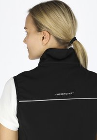 Schwarze ärmellose Weste mit hohem Kragen, ausgestattet mit einem weißen horizontalen Streifen und dem Logo "SWEDEMOUNT" auf dem Rücken. Glatte Textur.