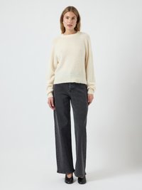 Maglione bianco, a trama, corto con maniche lunghe abbinato a jeans neri a vita alta e gamba dritta e scarpe nere senza lacci.
