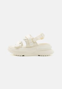 Sandalias gruesas en color blanco roto, con correas ajustables y una suela de plataforma texturizada con un dibujo profundo para mayor agarre.
