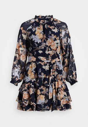 Laivastonsininen kukkamekko, jossa on pitkät läpikuultavat liehukehihat, röyhelöhame, korkea kaulus ja vyötärölle solmittava vyö.