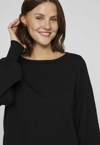 Pull en tricot noir avec un col large et des manches longues bouffantes. Texture douce, coupe décontractée et détails de conception minimalistes.