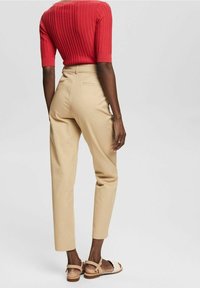 Top rosso a coste con maniche corte abbinato a pantaloni beige a vita alta e sandali color nocciola. Tessuto liscio e taglio su misura visibili dalla parte posteriore.