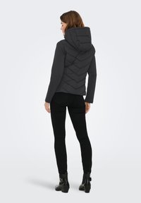 Μαύρο επενδυμένο μπουφάν με κουκούλα, σχέδιο ραφής chevron, μακριά μανίκια, συνδυασμένο με μαύρο παντελόνι και μποτίνια, από πίσω όψη.