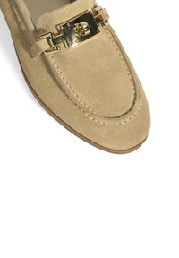 Beige suède instapper met een ronde neus, voorzien van een gouden gespaccent en zichtbare stiksels langs de randen. Gladde zool.