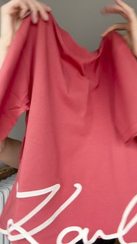 Camiseta de algodón roja con mangas cortas, presenta un dobladillo curvado y detalles de texto en blanco a lo largo del borde inferior. Tejido suave y liviano.