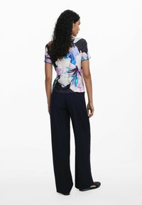 Top de manga corta con estampado floral que presenta colores vibrantes sobre un fondo oscuro, acompañado de pantalones anchos de color marino y zapatos negros planos.