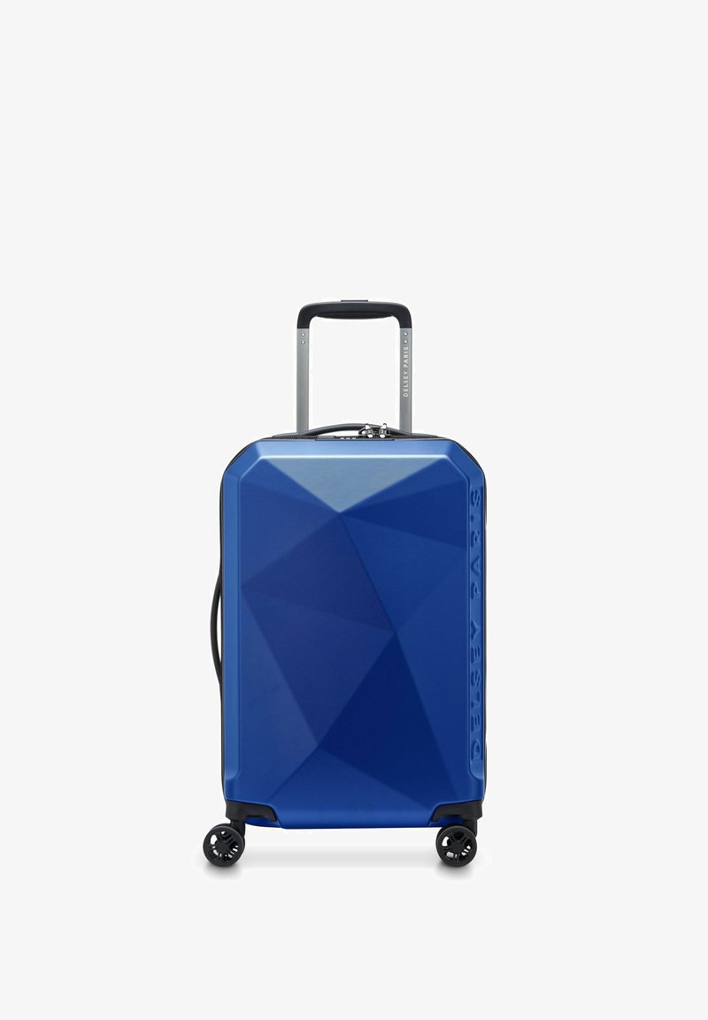 Valise rigide bleue au design angulaire, surface texturée, poignée télescopique et quatre roues noires pour la mobilité.