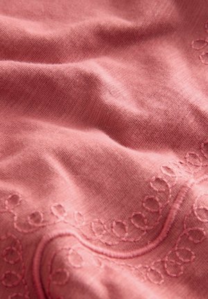 Roosa kangas pehmea tekstuuriga, mille servas on keerukad tikitud silmused. Materjal näeb välja sile ja veidi kortsus.