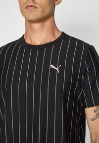 Sortstribet T-shirt lavet af bomuld, med hvide lodrette striber og et lille guld-logo på venstre brystområde. Rund halsudskæring.