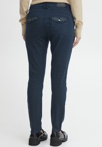 Marineblauwe slim-fit jeans met een middelhoge taille, voorzien van decoratieve studs op de achterzakken en een gladde, gestructureerde afwerking.