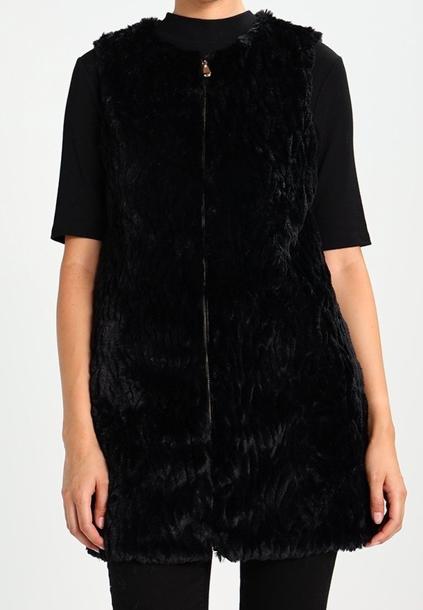 Svart faux pälsväst med hög krage och dragkedjeöppning. Har en texturerad yta och är ärmlös, kompletterad av en rak fåll.