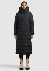 Lang sort dynejakke med høj krave, med knaplukning og en rektangulær lomme på brystet. Glat tekstur, knælængde.