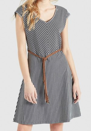 Femme portant une robe à rayures verticales noires et blanches avec un col en V et une ceinture tressée marron nouée à la taille.