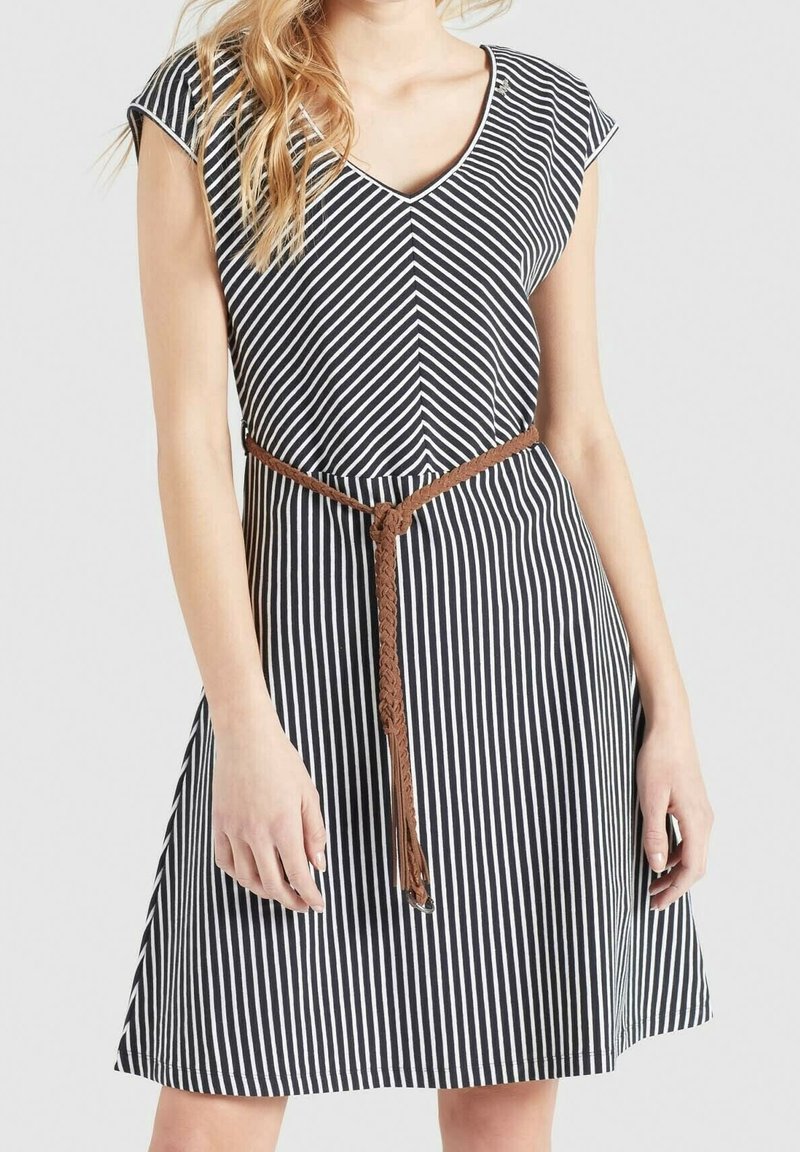 Femme portant une robe à rayures verticales noires et blanches avec un col en V et une ceinture tressée marron nouée à la taille.