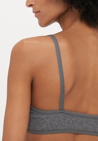 Szürke sportmelltartó vékony pántokkal, texturált anyagból, és varrat nélküli kivitelezéssel. Az alján található egy pánt, amely támogatást nyújt.