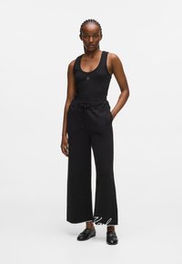 Melnā topiņš ar apaļu kakla izgriezumu un logotipu, apvienots ar platām melnām treniņu biksēm ar elastīgu vidukli un auklu. Melnas mokasīnas.