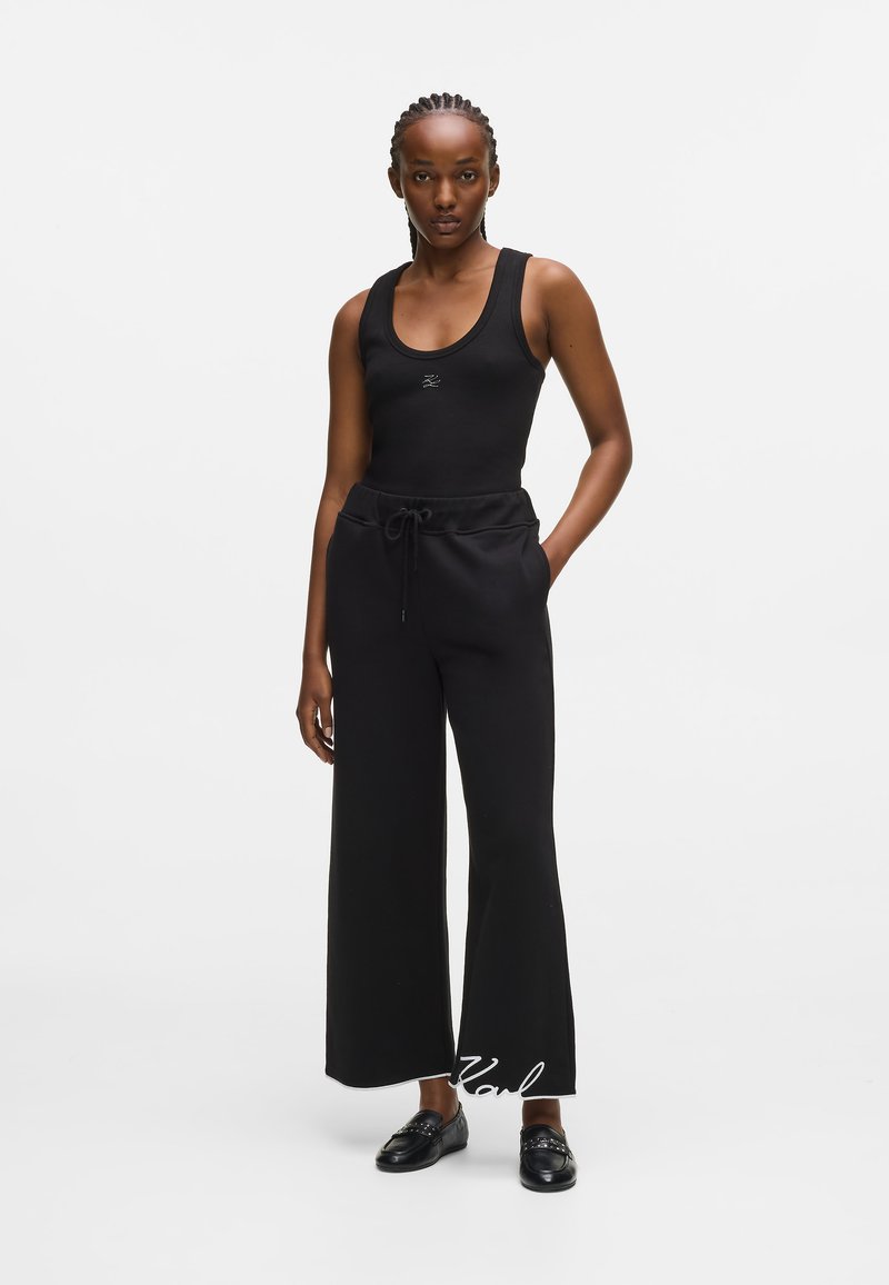 Melnā topiņš ar apaļu kakla izgriezumu un logotipu, apvienots ar platām melnām treniņu biksēm ar elastīgu vidukli un auklu. Melnas mokasīnas.