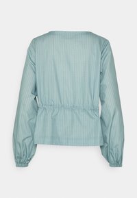 Blouse bleu clair à manches longues avec fines rayures verticales, taille et poignets élastiqués froncés, vue de dos sur fond blanc.