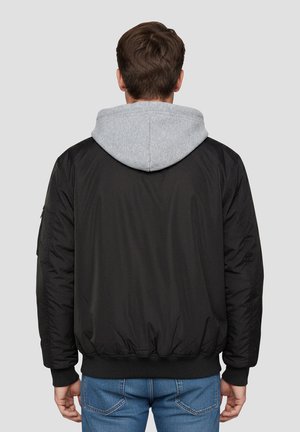 Zwarte bomberjack met grijze capuchon, geribbelde manchetten en taille, gestructureerde stof en zijzakken. Zichtbare stiksels op de mouwen.