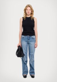 Top senza maniche lavorato a maglia nero, jeans azzurri decorati con motivi e una borsa nera. I jeans presentano dettagli con logo sul davanti. Le ballerine nere completano il look.